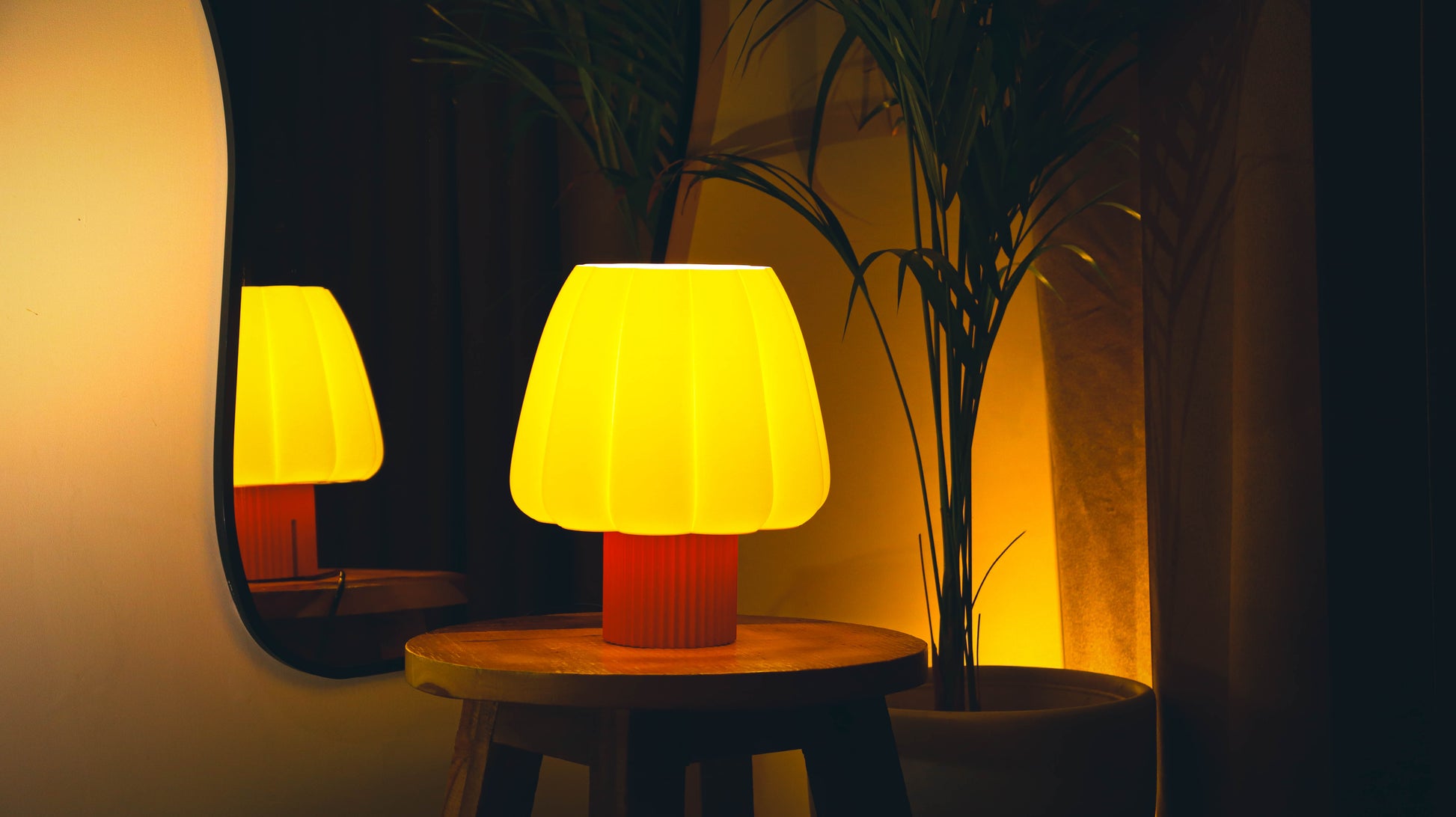 Marshmallow-style scalloped lamp shade glowing warm yellow on wood side table