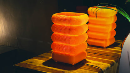 Mesh table lamp, orange stacked square design, illuminated on wooden table