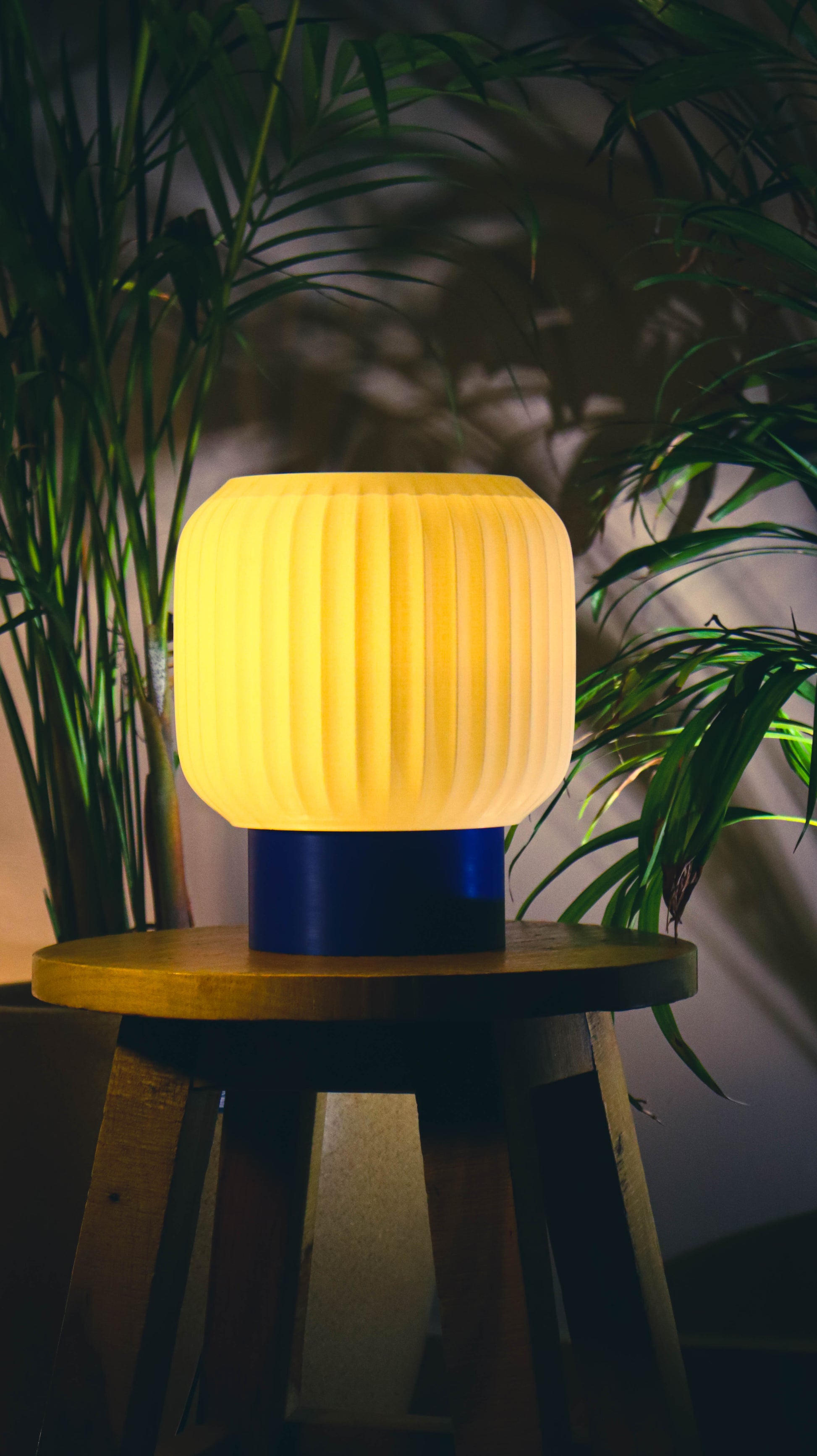 Yellow ribbed lamp on a wooden stool with plants in the background