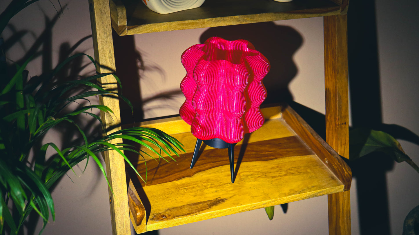 Pink wave-textured portable LED lamp with tripod legs on wooden shelf