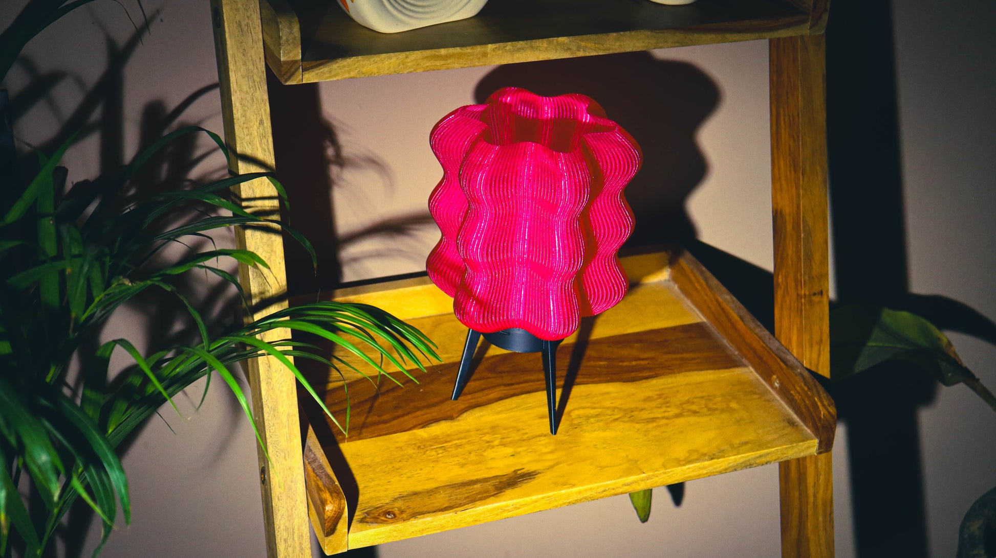 Pink wave-textured portable LED lamp with tripod legs on wooden shelf