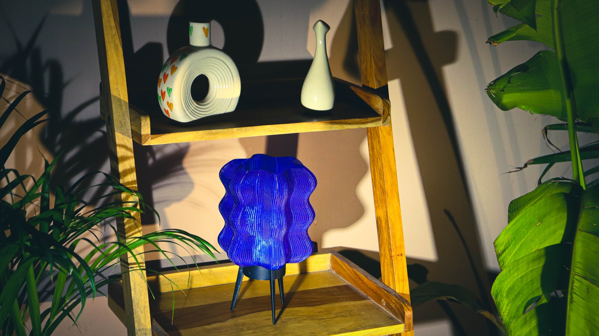 Blue lamp on a wooden shelf with decorative items and plants in a room.