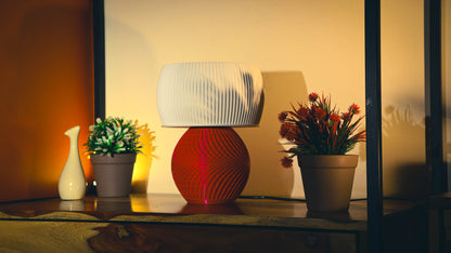 Decorative table with a red lamp, small plant, and larger flower arrangement against a neutral wall.