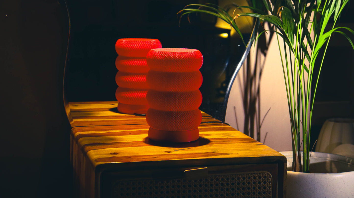 Bold red stacked ring lamps glowing on wood surface, plant backdrop