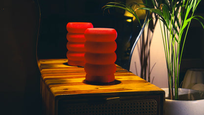 Bold red stacked ring lamps glowing on wood surface, plant backdrop